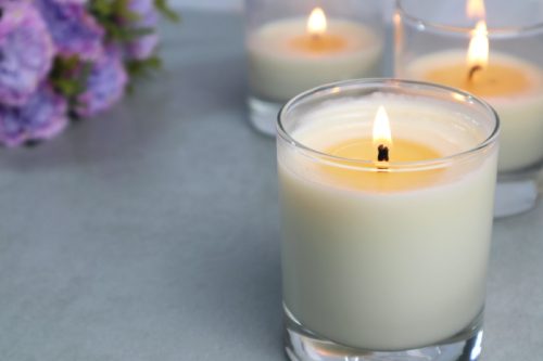 close up of candle in glass container burning with two candles behind it