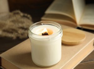 candle with wood wick burning on a book next to another book