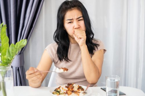 young woman coughing as she chokes while eating