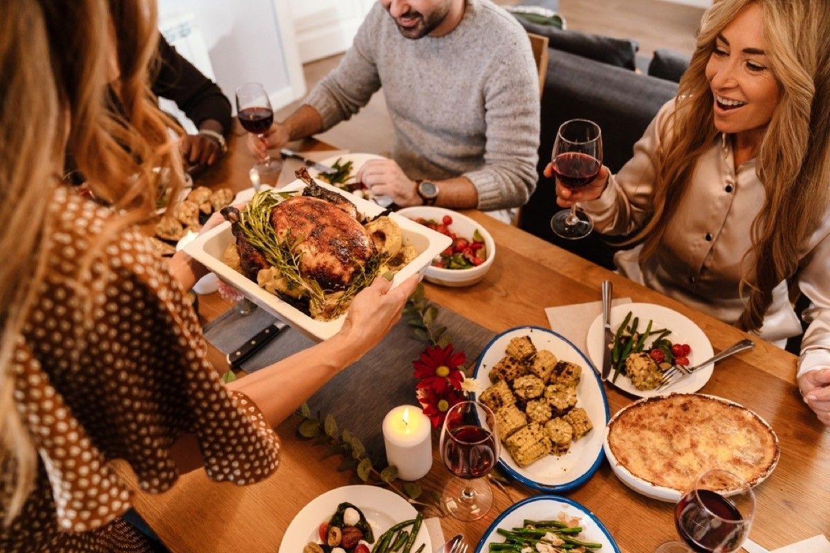 turkey being served at thanksgiving with plates of sides on the table