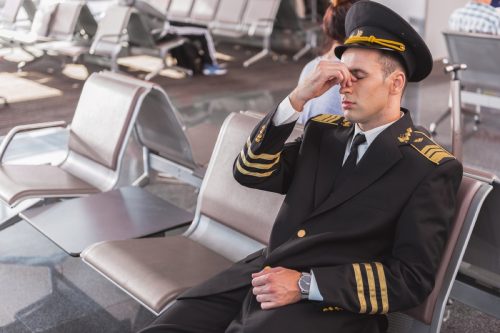 tired pilot pinching the bridge of his nose while seated at an airport