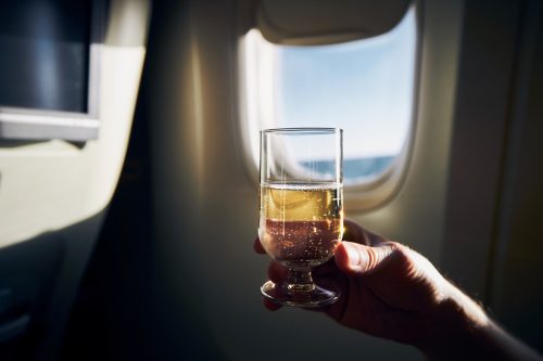 Man holding glass of sparkling wine against airplane window.