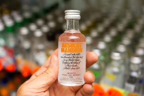 A hand holds a miniature liquor bottle, featuring the brand name Absolut Mandrin