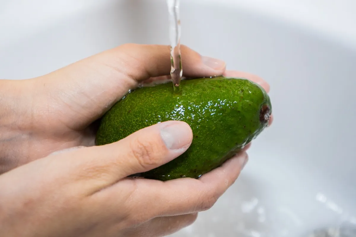 person washing avocado with water
