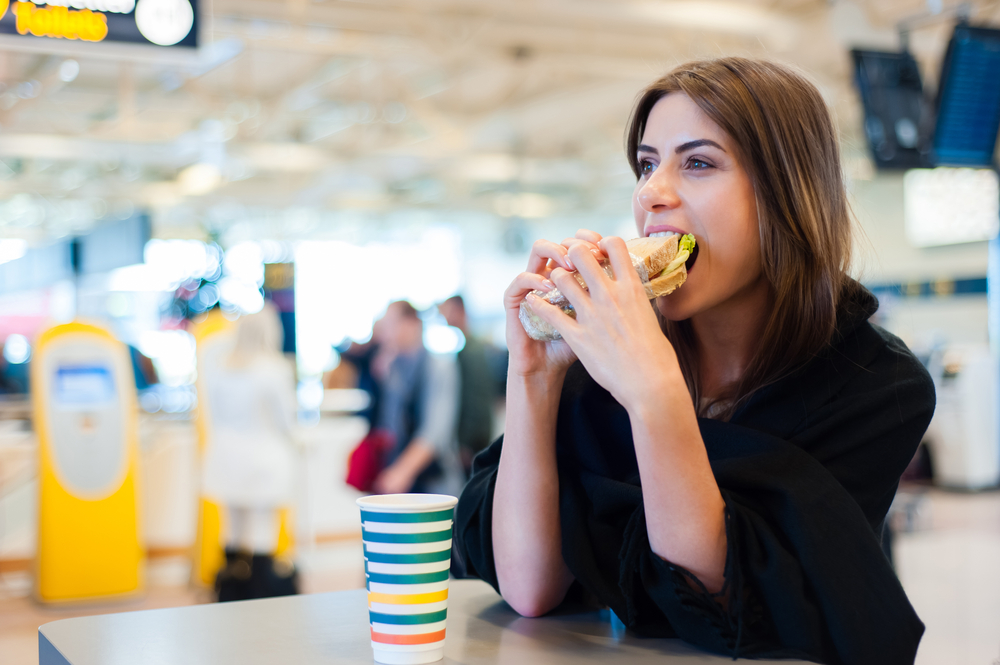 Junge Frau, die am Flughafen ein Sandwich isst
