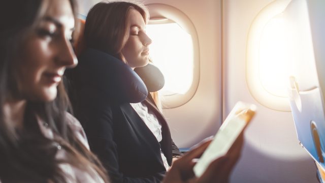 A woman sleeping on a plane with a neck pillow