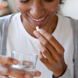 A young woman taking a supplement pill with a glass of water