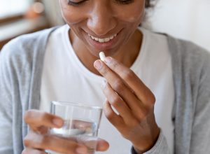 A young woman taking a supplement pill with a glass of water