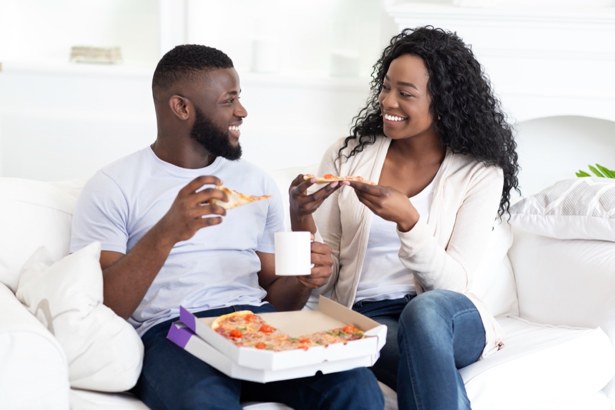 young happy couple eating pizza in modern apartment