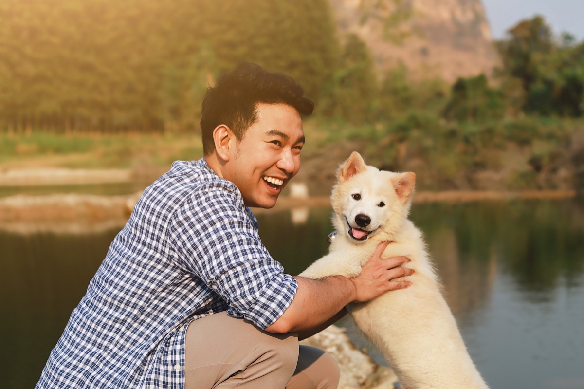 young smiling man playing with pet dog near lake