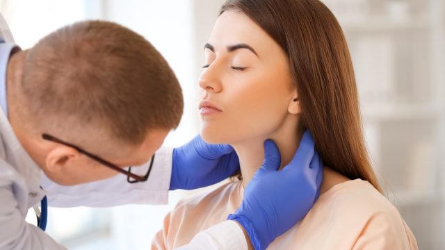 Doctor examining young woman's neck