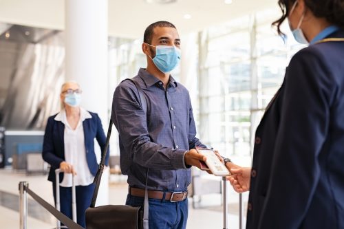 passenger wearing surgical mask showing e-ticket to flight attendant at boarding gate