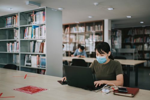 Ein College-Student, der in einer Bibliothek studiert und soziale Distanzierung beobachtet