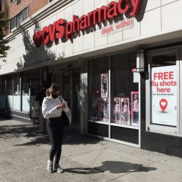 Manhattan, New York. October 08, 2020. A woman wearing a face mask walks in front of a CVS pharmacy Midtown with a sigh advertising free flu shots.