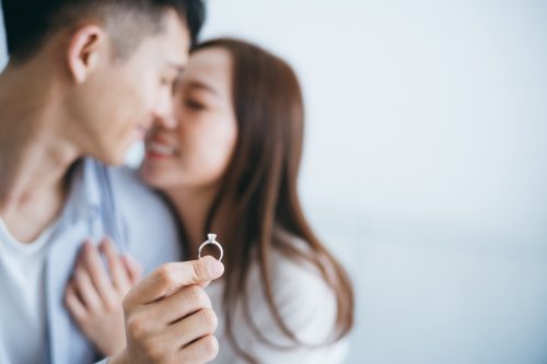 A man with an engagement ring proposes to his girlfriend in a new house, they kiss with a smile