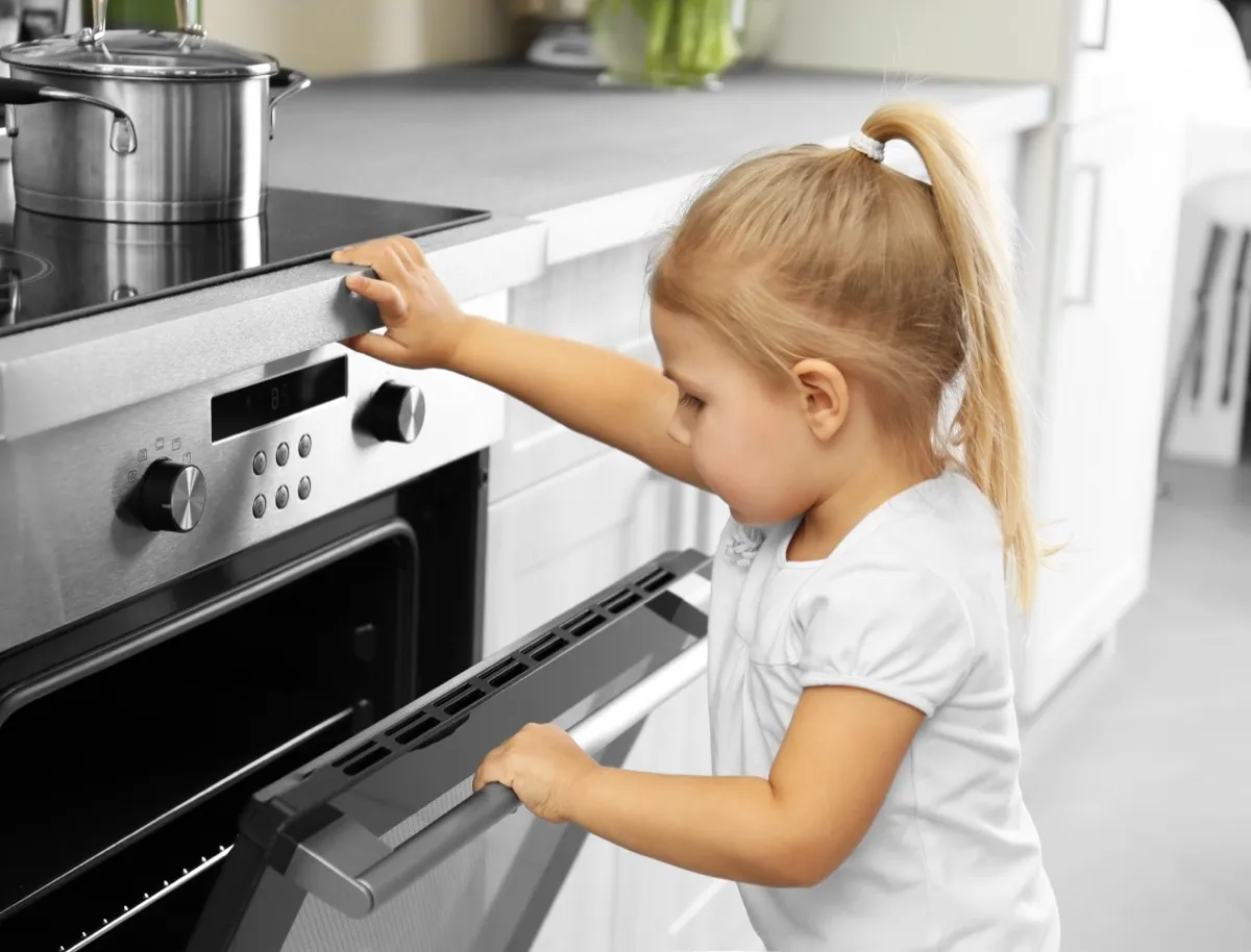 small blonde child in ponytail opening door to stove