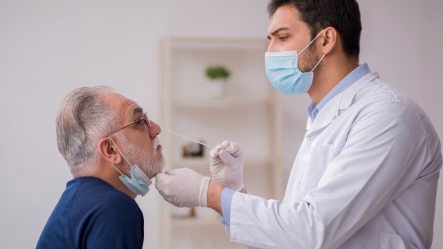 A senior man getting a COVID nasal swab test from a doctor or healthcare worker