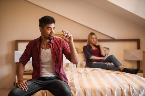 Man drinking beer on bed and woman next to him