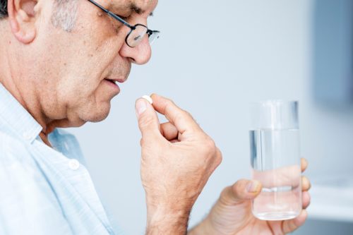 A senior man taking medication with a glass of water