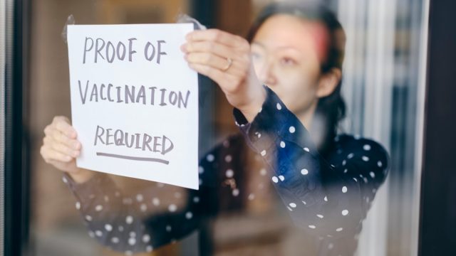 A business owner putting up a sign requiring proof of vaccination.