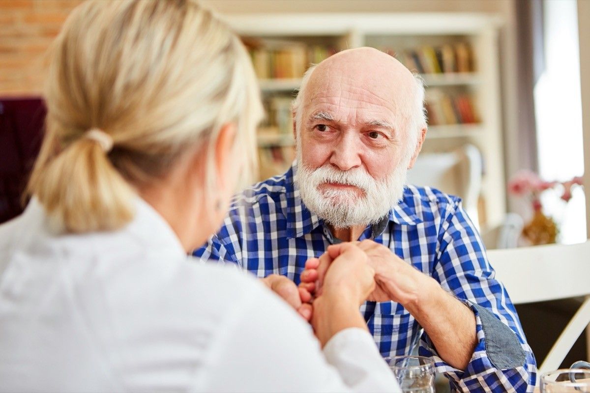 older man with dementia holding hands with doctor