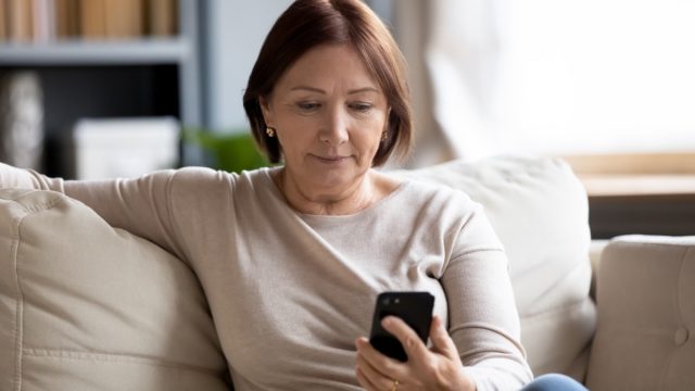 middle-aged woman sitting on couch holding smartphone