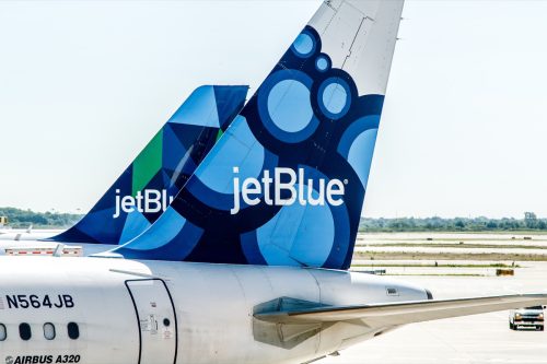 Two JetBlue airplanes are parked by the gates awaiting passenger boarding.