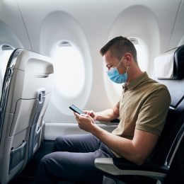 Man wearing face mask and using phone inside airplane during flight. Themes new normal, coronavirus and personal protection.