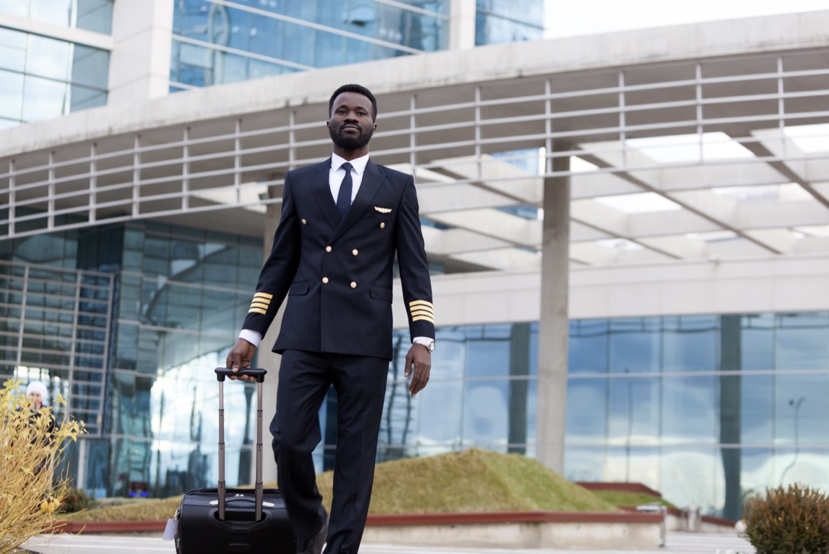 Un pilot de avion își trage bagajele în terminalul aeroportului