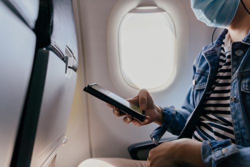 20s young adult male tourist wearing a face mask inside aircraft cabin air. and using a cell phone. Public transportation during Covid-19 or Coronavirus pandemic.