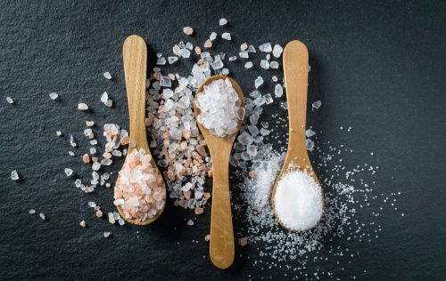 Different types of salt. Sea, himalayan and kitchen salt. Top view on three wooden spoons on black background