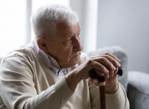 A senior man sitting on the couch and holding a cane