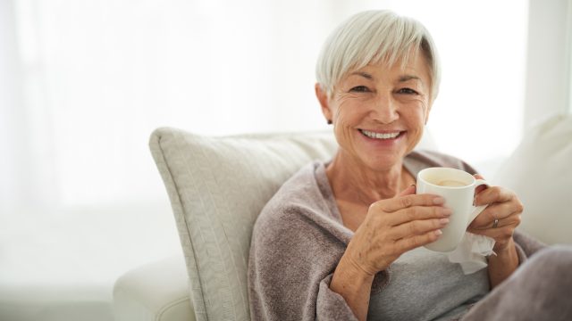 A senior woman sitting on the sofa drinking a cup of coffee
