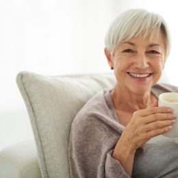 A senior woman sitting on the sofa drinking a cup of coffee