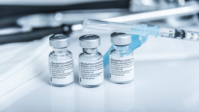 Three vials of Pfizer COVID-19 vaccine with a syringe beside them