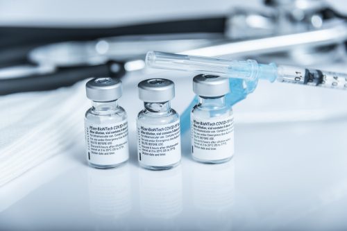 Three vials of Pfizer COVID-19 vaccine with a syringe beside them