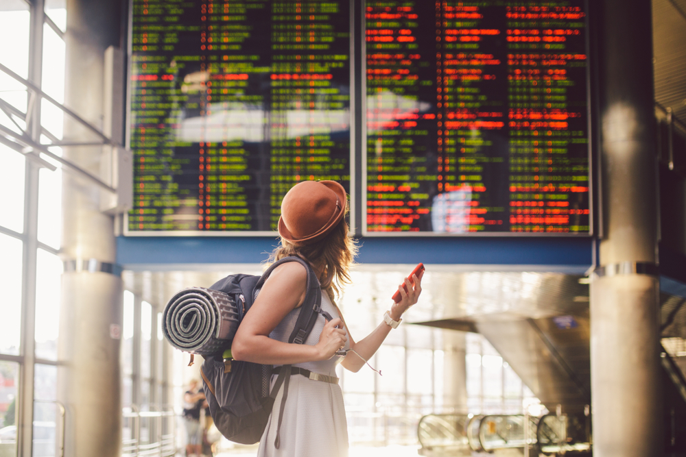 A woman at the airport checking when her flight leaves while carrying her luggage