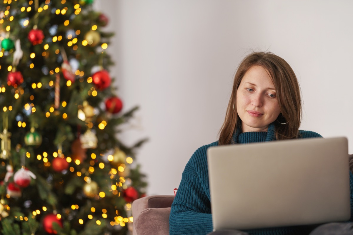 woman shopping on a laptop with a christmas tree behind her