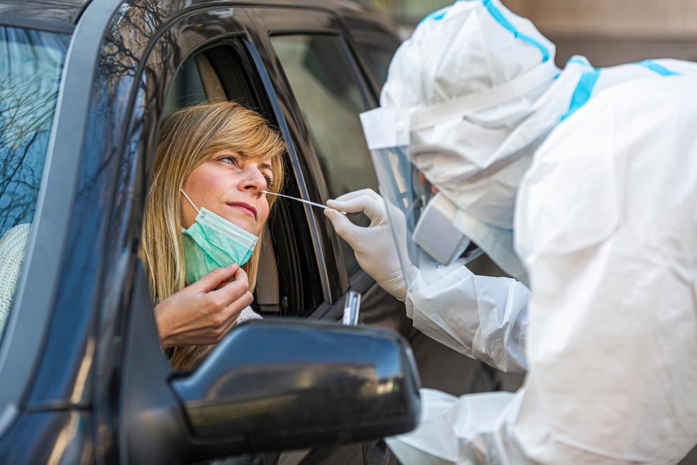 A woman getting a COVID test nasal swab from a healthcare worker while seated in her car