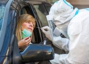 A woman getting a COVID test nasal swab from a healthcare worker while seated in her car