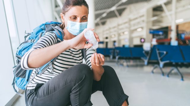 A woman wearing a face mask using hand sanitizer in an airport terminal