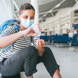 A woman wearing a face mask using hand sanitizer in an airport terminal