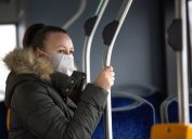 A young woman wearing a face mask while riding a public bus