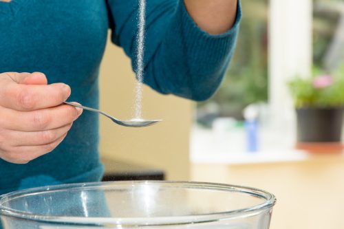 Woman measuring a teaspoonful of salt over a glass bowl