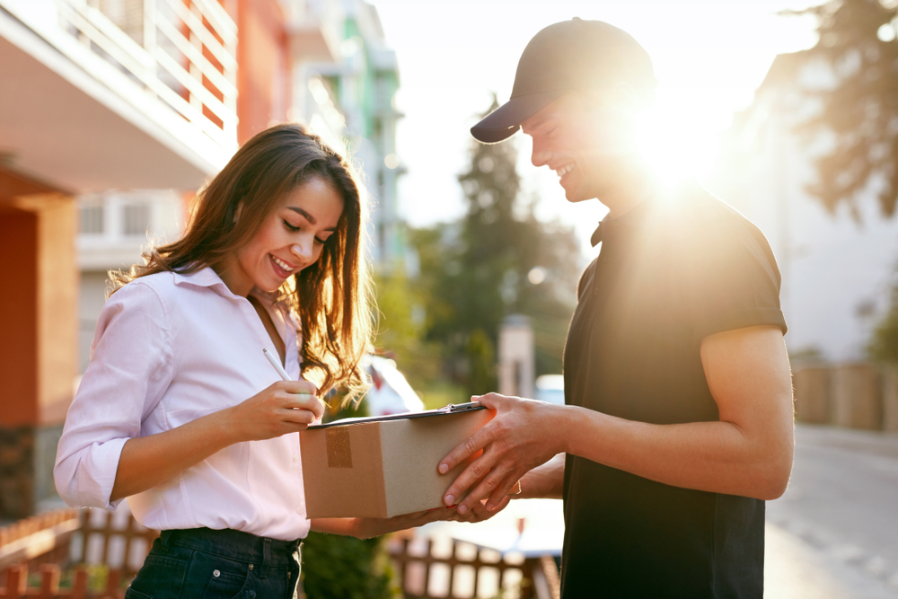 A young woman signing for a package being delivered to her by a courier