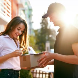 A young woman signing for a package being delivered to her by a courier
