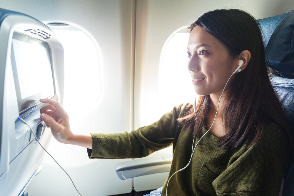A woman using the in-flight entertainment on a plane while wearing earbuds
