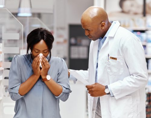 Shot of a woman blowing her nose while being assisted by a pharmacist in a chemist