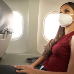 A young woman seated on an airplane wearing a face mask