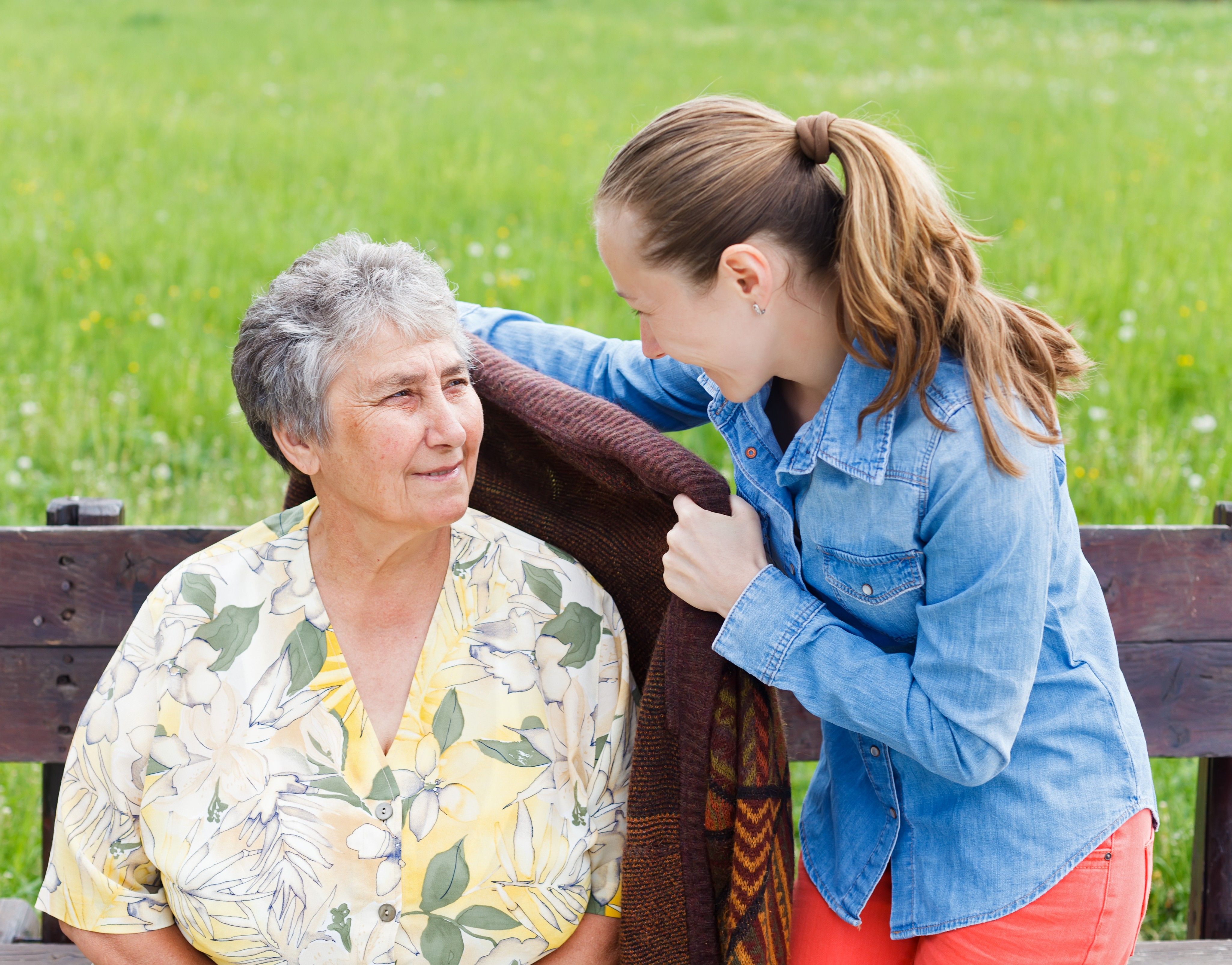 Young woman putting coat on elderly woman